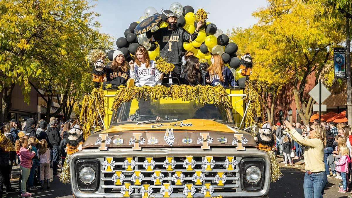 An old truck driving through downtown Moscow during the Homecoming parade with people taking pictures of it